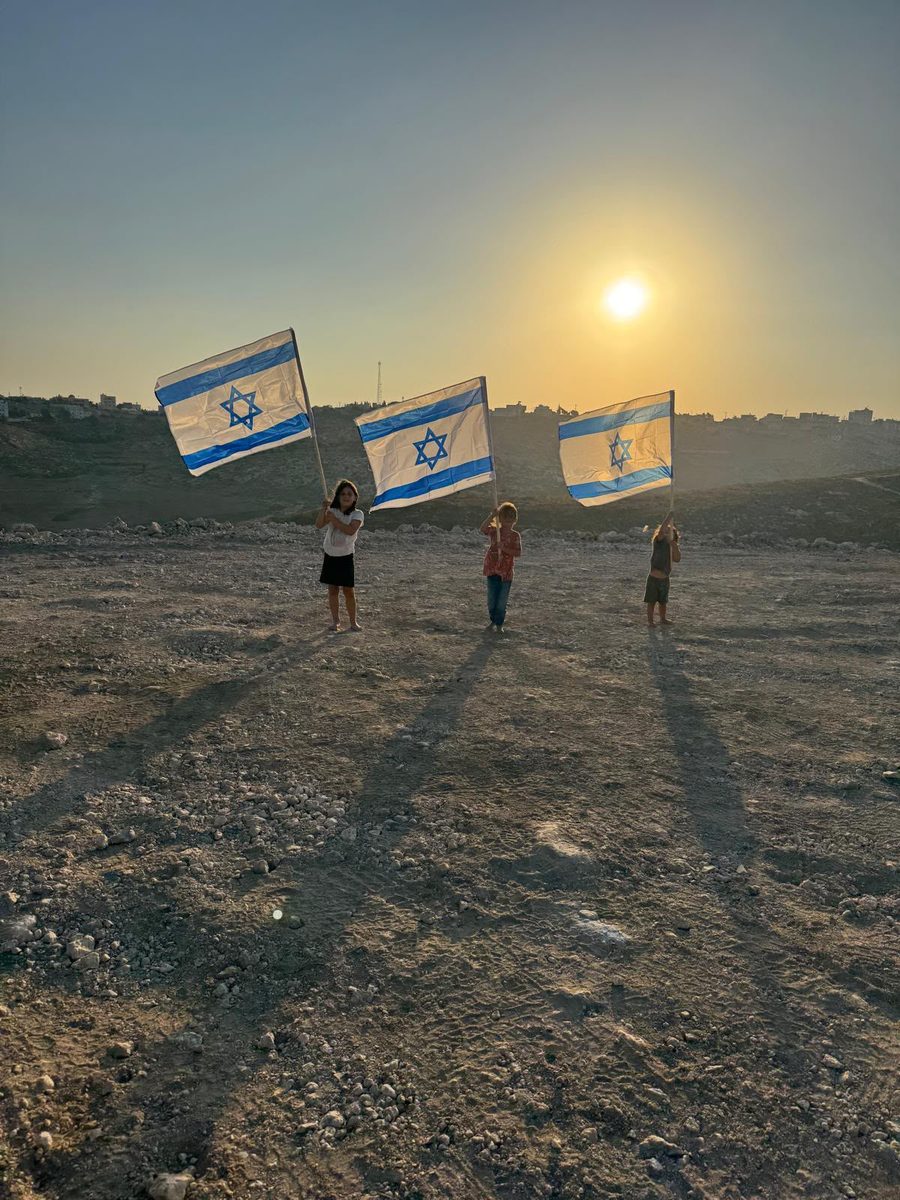 ילדי המשפחה מניפים דגלי ישראל על אדמת החווה